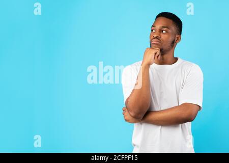Pensieroso uomo africano pensare guardando da parte posando su sfondo blu Foto Stock
