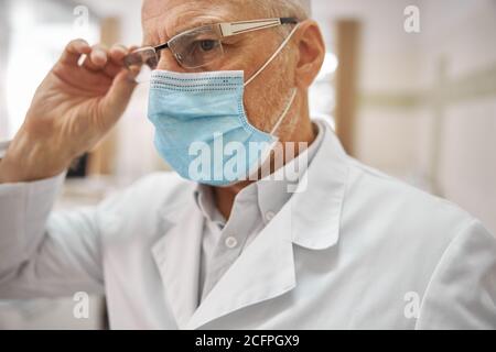 Uomo anziano che indossa una maschera e occhiali che lavorano in clinica Foto Stock