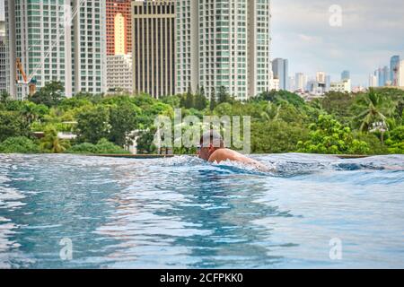 Manila, Filippine - Feb 02, 2020. Un uomo nuota un colpo di seno in una piscina sul tetto di un hotel di lusso. Vista della città di Manila dalla piscina di Foto Stock