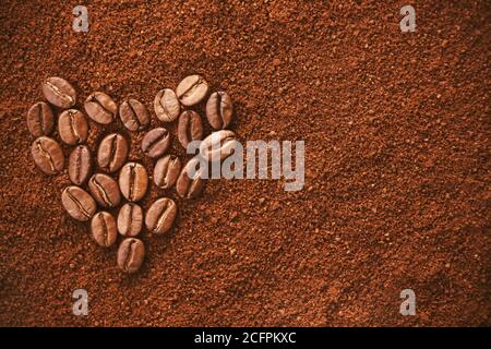 Sullo sfondo del caffè macinato, il simbolo del cuore è rappresentato dai chicchi di caffè aromatici tostati. Amore per il caffè. Bevanda rinvigorente preferita. Foto Stock