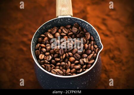 Sullo sfondo del caffè macinato si trova una bella cezve puntinata di blu, per preparare il caffè, completamente riempito con chicchi di caffè tostati. Preferito Foto Stock