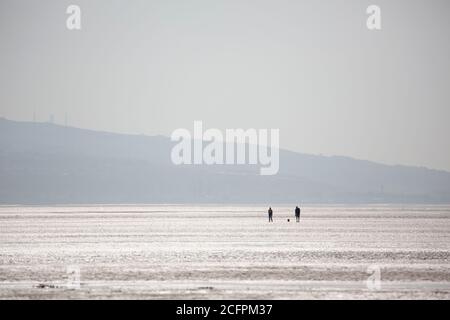 Due persone che camminano il loro cane sulla spiaggia di West Kirby Foto Stock