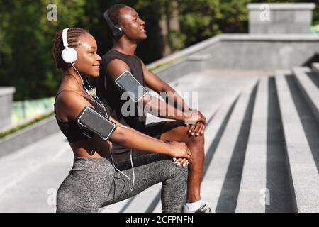 Coppie africane sportive che fanno esercizi di stretching all'aperto nel City Park, vista laterale Foto Stock