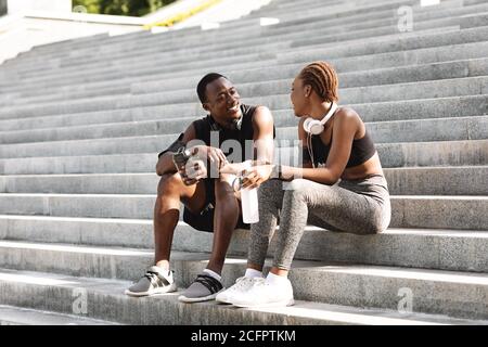 Coppia africana positiva che riposa dopo l'allenamento fitness all'aperto, seduto su gradini urbani Foto Stock