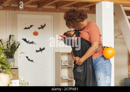 Madre amorevole baciare il suo figlio carino indossando costume diavolo con corna rosse prima di lasciarlo uscire per trucco o. trattare con altri bambini Foto Stock