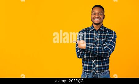 Cheerful Black Guy in posa puntando la barretta da parte in Studio, Panorama Foto Stock