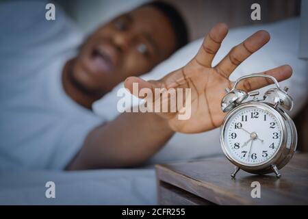 Black Guy disattivazione della funzione di allarme-orologio che si trova nel letto interno Foto Stock