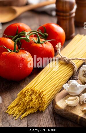 Spaghetti crudi legati in un fascio di vite fresca pomodori e aglio su un rustico tavolo di legno Foto Stock