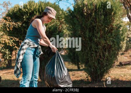 Il concetto di inquinamento ambientale e giorno della Terra. Una volontaria femminile pulisce il Parco, raccogliendo i sacchi per la spazzatura in un unico luogo. Primo piano. Foto Stock