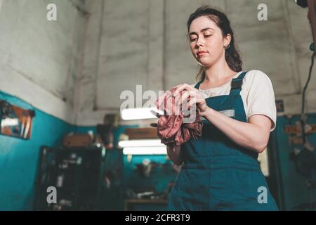 Uguaglianza di genere. Ritratto di una giovane donna in uniforme, che lavora in un laboratorio, che gli strofina le mani con uno straccio. Vista dal basso. Negozio auto nel backgrou Foto Stock