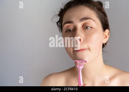 Una giovane donna graziosa sta provando a radere il suo mento con un machine.The concetto di sbarazzarsi dei capelli indesiderati. Spazio di copia. Foto Stock