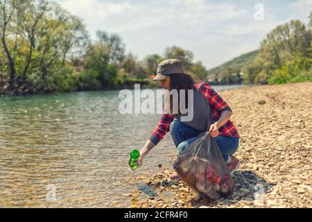 Una donna volontaria tira una bottiglia fuori dall'acqua, durante l'evento per pulire la riva del fiume. Concetto di miglioramento della giornata della terra e dell'ambiente. Foto Stock