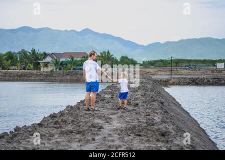 Padre figlio camminare vicino lago di montagna, guardare l'un l'altro winking. Felice infanzia. L'educazione naturale del bambino domestico, giorno dei padri, responsabilità del papà Foto Stock