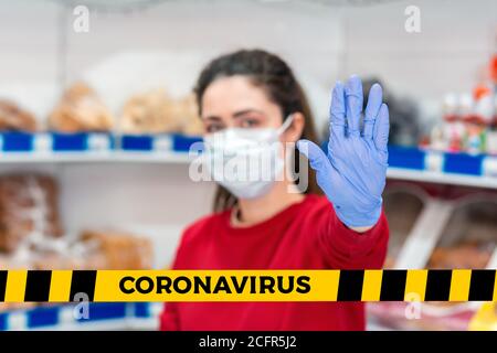 Non incrociare.nastro barriera-quarantena,isolation.UNA donna in guanti di gomma e una maschera medica che tiene in su un segno di stop. Sullo sfondo sono le mensole di Th Foto Stock