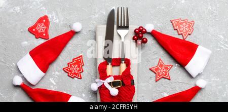 Set festivo di forchetta e coltello su fondo cementizio. Banner vista dall'alto delle decorazioni del nuovo anno e abiti e cappello santa. Primo piano del concetto di Natale. Foto Stock