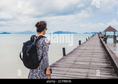 Donna in estate vestito a piedi su ponte di legno con mare tranquillo. Foto Stock