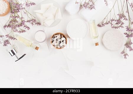 Prodotti e accessori di bellezza beige naturale delicato per il bagno con fiori secchi viola su fondo bianco chiaro morbido, posa piatta, spazio copia, bordo. Foto Stock