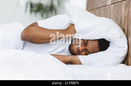 Uomo disturbato che copre le orecchie con cuscino sofferente da Insomnia Indoor Foto Stock