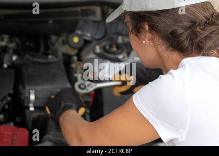 Forza lavoro donna. Lavoratrice meccanica auto femminile sul motore dell'automobile usando un arpionismo. Servizio di riparazione. Primo piano autentico. Giorno del lavoro. Foto Stock