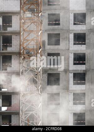 Vista della facciata di un edificio monolitico in cemento a più piani in costruzione. Recinzioni e strutture metalliche sui pavimenti. La polvere di cemento sta volando Foto Stock
