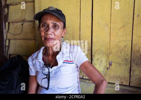 Kota Kinabalu / Malesia - 13 gennaio 2019: Ritratto di donna malese adulta seduta indossando un cappuccio di fronte a muro di legno con polo bianca camicia nel villaggio galleggiante Kampung Tanjung Aru lama Foto Stock