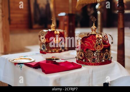 Due belle corone con oro e stoffa rossa si levano in piedi una tavola nella chiesa prima del battesimo del bambino Foto Stock