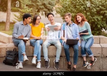 Asian Guy che mostra il progetto sul tablet ai compagni-studenti seduti all'aperto Foto Stock
