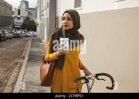 Donna che tiene una tazza di caffè mentre cammina in bicicletta Foto Stock