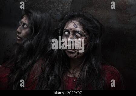 donna con capelli lunghi travestita da zombie, riflettendo in uno specchio, con sfondo scuro, orrore Foto Stock