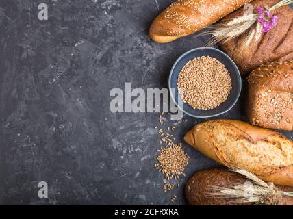 Diversi tipi di pane appena sfornato su fondo nero in cemento. Vista dall'alto, disposizione piatta, spazio per la copia. Foto Stock