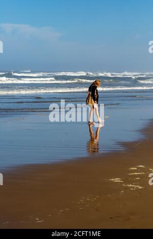 Donna che cammina su una spiaggia accanto all'oceano in Oregon alla ricerca di conchiglie, verticale Foto Stock