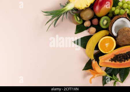 Vista di una composizione con varietà di frutta tropicale fresca e foglie disposte su una superficie rosa Foto Stock