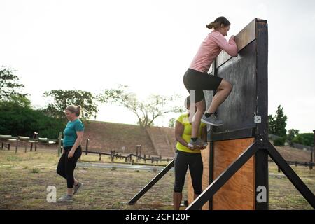 Donna che si arrampica su un muro di ostacolo al campo di stivali Foto Stock