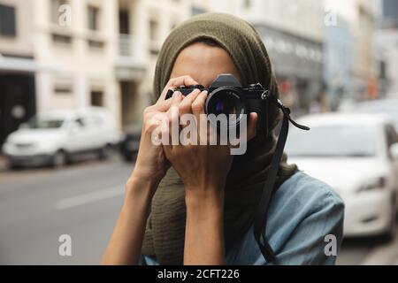 Donna in hijab che scatta foto utilizzando la fotocamera digitale sul via Foto Stock