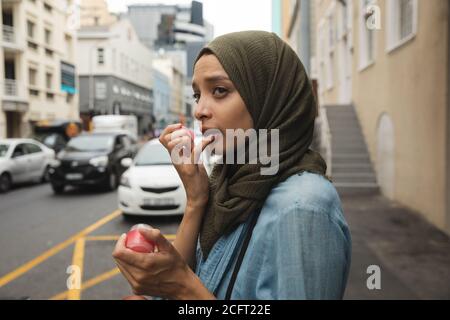 Donna in hijab che applica il balsamo del labbro sulla strada Foto Stock