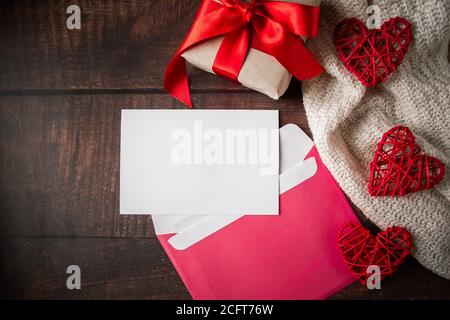 Busta e biglietto d'auguri su sfondo di legno. Lettera di congratulazioni per San Valentino in busta rosa. Dono e cuori rossi sullo sfondo di Foto Stock