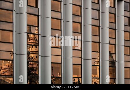 Il Bastione dei pescatori di Budapest si riflette nel vetro dorato finestre di un moderno edificio d'affari Foto Stock