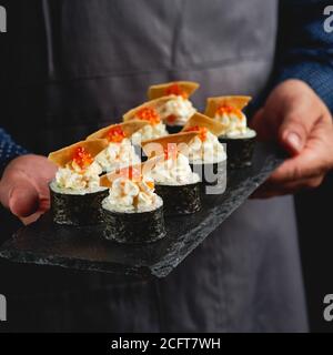Sushi roll maki futo cibo giapponese su un piatto di pietra nera nelle mani di un cameriere. Primo piano Foto Stock