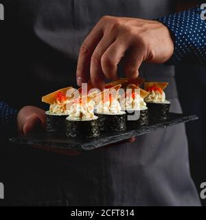 Sushi roll maki futo cibo giapponese su un piatto di pietra nera nelle mani di un cameriere. Primo piano Foto Stock