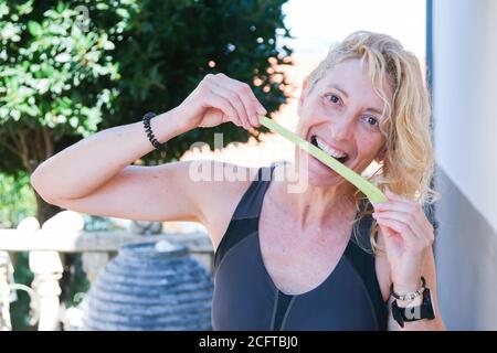 Giovane bionda matura in abbigliamento sportivo che batte un gambo di sedano all'aperto Foto Stock