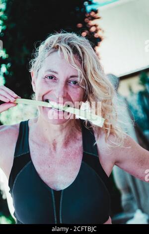 Giovane bionda matura in abbigliamento sportivo che batte un gambo di sedano all'aperto Foto Stock