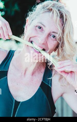 Giovane bionda matura in abbigliamento sportivo che batte un gambo di sedano all'aperto Foto Stock