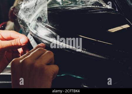 Primo piano dell'installazione della pellicola di protezione della vernice sullo specchietto laterale della moderna auto di lusso. Il PPF è una pellicola di poliuretano applicata alla vernice dell'auto per proteggere il Foto Stock