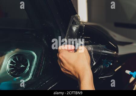 Primo piano dell'installazione della pellicola di protezione della vernice sullo specchietto laterale della moderna auto di lusso. Il PPF è una pellicola di poliuretano applicata alla vernice dell'auto per proteggere il Foto Stock