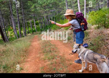 Giovane donna matura escursionista con un cappello e un cane in un percorso. Foto Stock