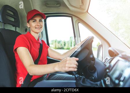 servizi di trasporto - giovane autista donna in uniforme rossa che guida un furgone. sorridendo alla macchina fotografica Foto Stock