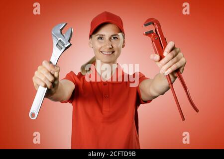 handyman services - donna maneggevole in uniforme rossa con riparazione strumenti in mani su sfondo rosso Foto Stock