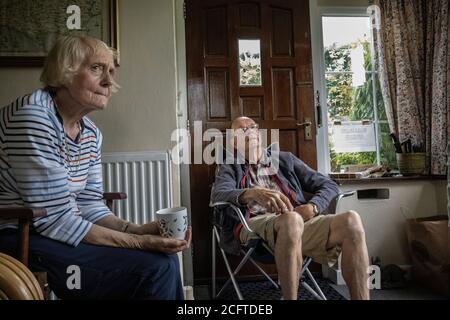 La coppia anziana si sedette nel loro portico a distanza sociale a casa durante il blocco pandemico del coronavirus, Galles, Regno Unito Foto Stock