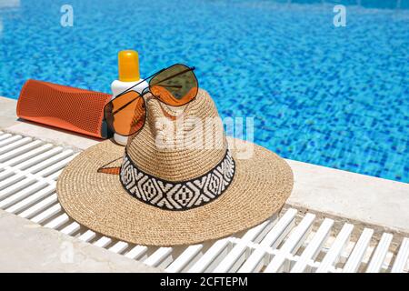 accessori da spiaggia di colore arancione vicino alla piscina. Crema solare, occhiali da sole, altoparlante e cappello di paglia Foto Stock