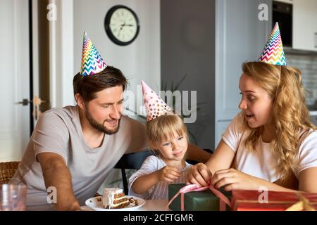 bambina caucasica in attesa di ricevere, disimballaggio doni dai genitori. adorabile ragazza felice celebrare il compleanno a casa con la famiglia Foto Stock